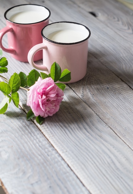 Zwei rosa Tassen mit Milch auf dem weißen Holztisch