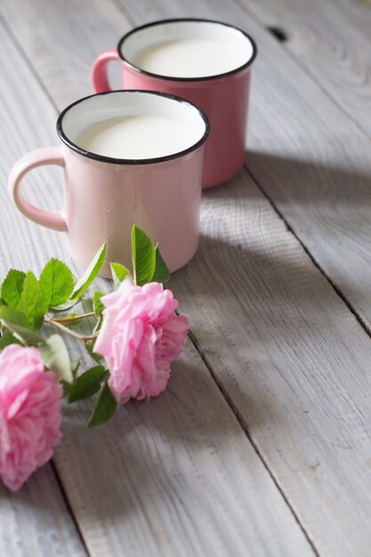Zwei rosa Tassen mit Milch auf dem weißen Holztisch