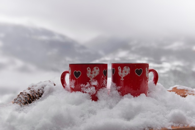 Zwei rote Becher mit Herz geformt auf dem Schnee- und Berghintergrund-Valentinsgrußkonzept