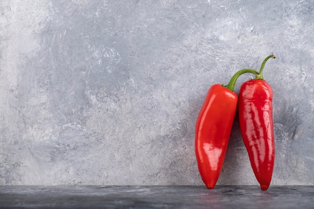 Zwei rote Chilischoten auf Marmoroberfläche.