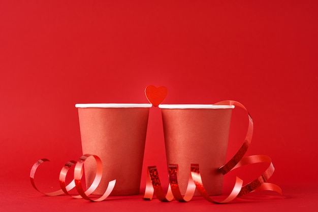 Zwei rote Papierkaffeetasse und Herz auf roter Oberfläche. Romantik und Valentinstag Konzept