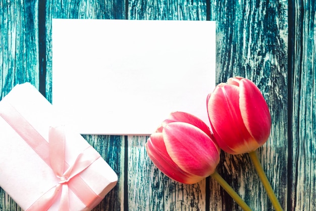 Zwei rote Tulpen Geschenkkiste und weiße Mockup Leer auf blauem Holzgrund Ostern Muttertag oder Frauentag Grußkarte Kopieren Sie Platz für den Text