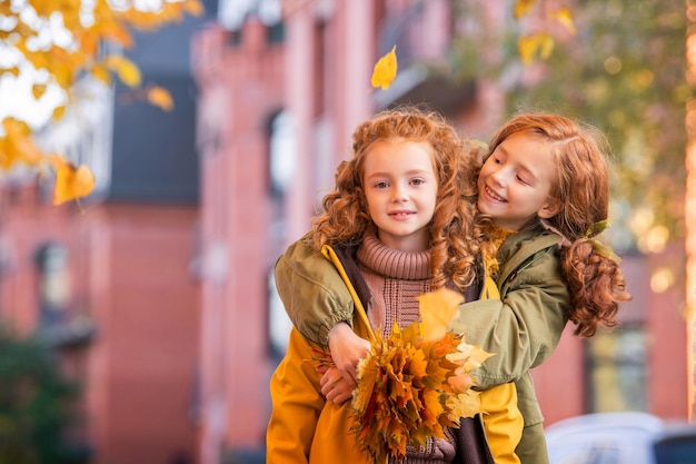 Zwei rothaarige Mädchenschwestern gehen während des goldenen Herbstlaubfalls fröhlich die Stadtstraße entlang