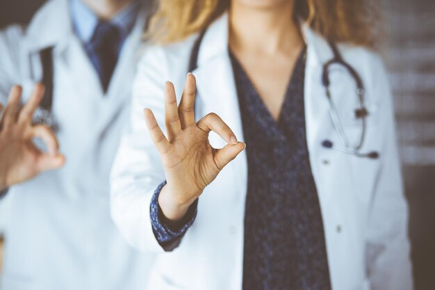 Zwei Ärzte stehen mit OK-Schild im Krankenhausbüro. Medizinische Hilfe, Bekämpfung von Virusinfektionen und Medizinkonzept.