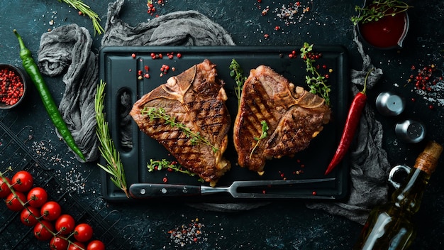 Zwei saftig gegrillte Steaks mit Gewürzen und Kräutern auf schwarzem Hintergrund. Ansicht von oben. Rustikaler Stil.