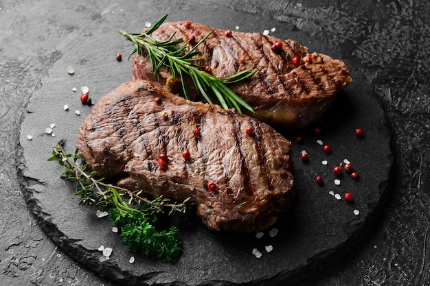 Zwei saftige Rib-Eye-Steakkräuter und Gewürze auf schwarzem Steinhintergrund