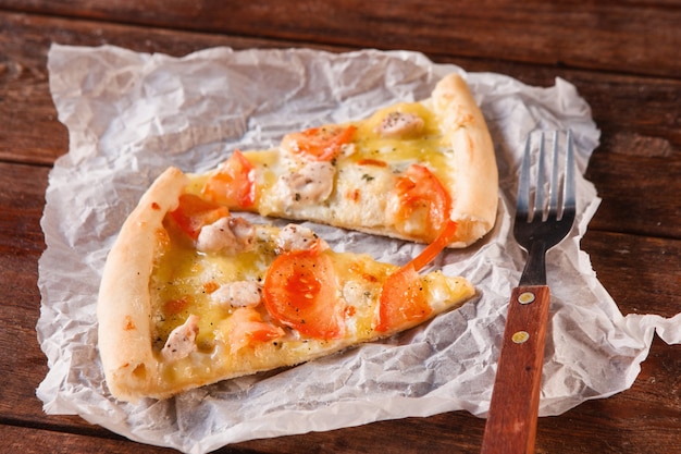 Zwei Scheiben frisch gebackene Pizza auf weißer Papierserviette mit Gabel, Nahaufnahme. Italienisches Essen, schnelles Mittagessen auf rustikalen dunklen Holztisch serviert.