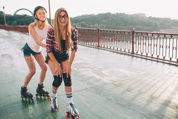 Zwei schlanke und sexy junge Frauen und Rollschuhe. Eine Frau hat Inline-Skates und die andere Quad-Skates. Mädchen reiten in den Strahlen der Sonne.