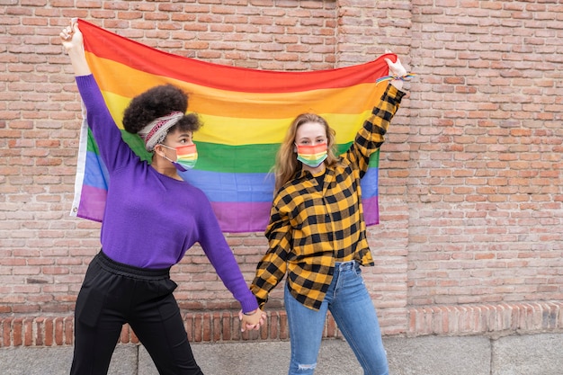 Zwei schöne afrikanische und kaukasische Frauen mit Gay-Pride-Flagge