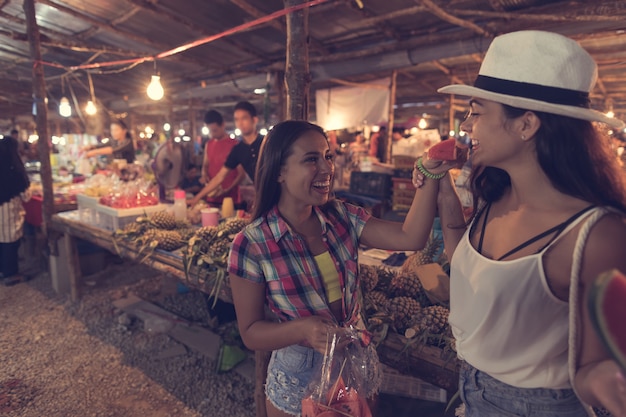 Zwei schöne Frauen, die Wassermelone auf traditionellem Straßenmarkt in Asien schmecken