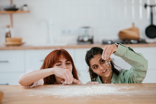 Zwei schöne Frauen spielen in der Küche mit Mehl