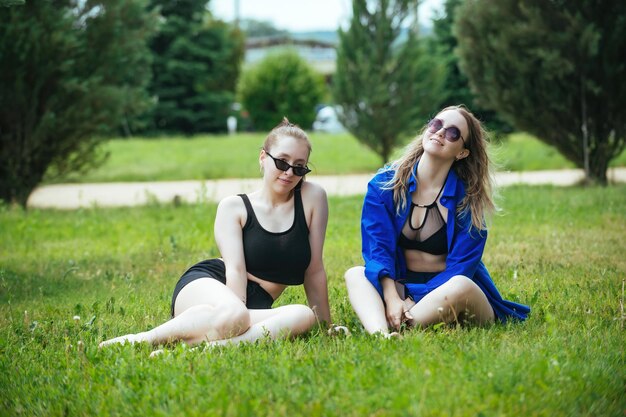 Zwei schöne Freundinnen haben Spaß und posieren im Sommer im Urlaub auf einer grünen Wiese