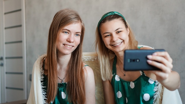 Zwei schöne glückliche Freundinnen, die Selfie mit Smartphone auf Pyjama-Party nehmen