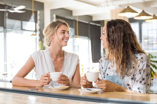 Zwei schöne junge Frauen, die eine Tasse Kaffee halten und miteinander sprechen