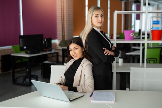 zwei schöne junge Frauen im Büro mit einem Laptop