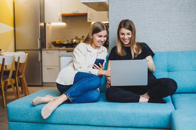 Zwei schöne junge Frauen mit Laptop Film auf dem Sofa zu Hause sitzen zwei Freundinnen sitzen auf dem Sofa zu Hause im Wohnzimmer