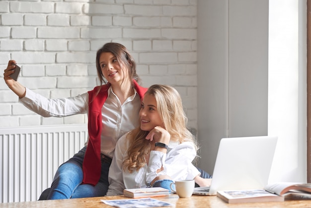 Zwei schöne junge Freundinnen nehmen Selfies zusammen im Café unter Verwendung der Smartphone-Copyspace-Freundschaft Menschen Teenager Jugendtechnologie Erinnerungen Emotionen Zusammengehörigkeit Bindung.