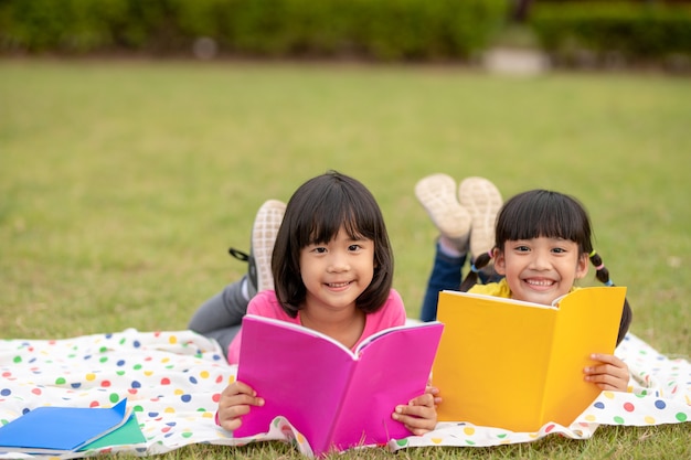 Zwei schöne kleine Mädchen, die Bücher im Garten lesen, sitzen auf Gras. Das Konzept der Bildung und Freundschaft.