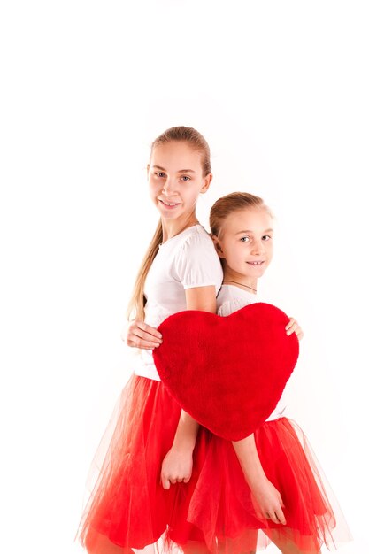 Zwei schöne Mädchen, die rotes Herz lokalisiert halten. St. Valentinstag, Liebe und Glück Konzept.