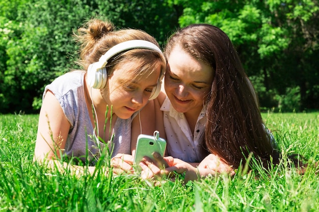Zwei schöne Mädchen, jünger und älter, lernen Fremdsprachen auf dem Rasen im Stadtpark