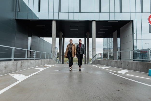 Zwei schöne stilvolle junge Frauen in modischer Herbstkleidung gehen in der modernen Stadt die Straße entlang