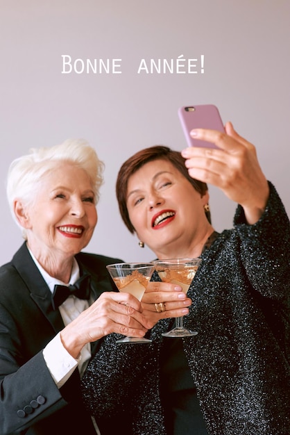 Zwei schöne, stilvolle, reife ältere Frauen, die Wein trinken und ein Selfie-Foto machen. Lustige Party-Technik