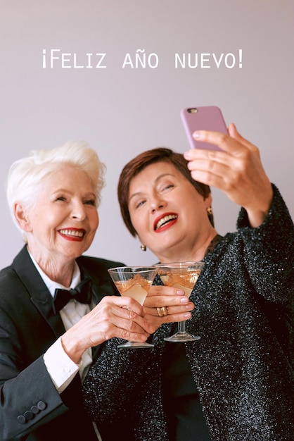 Zwei schöne, stilvolle, reife ältere Frauen, die Wein trinken und ein Selfie-Foto machen. Lustige Party-Technik