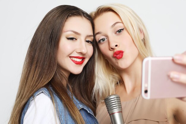 Zwei Schönheitsmädchen mit Mikrofon machen Selfie mit Smartphone