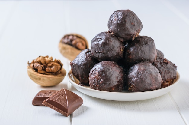 Zwei Schokoladenstücke, zwei Walnüsse und hausgemachte Trockenfruchtbonbons auf einem weißen Holztisch. Leckere frische hausgemachte Süßigkeiten.