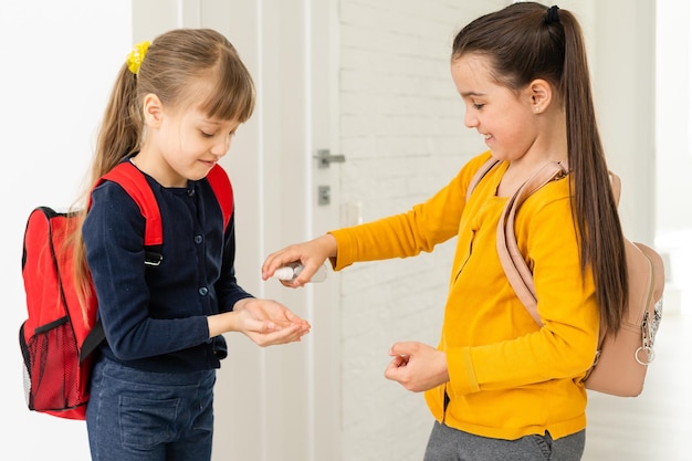 Zwei Schulmädchen wenden im Klassenzimmer Händedesinfektionsmittel an.