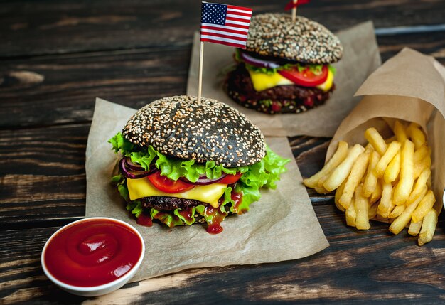 Zwei schwarze Hamburger mit amerikanischer Flagge, Salat, Tomate und Pommes Frites. Holzhintergrund