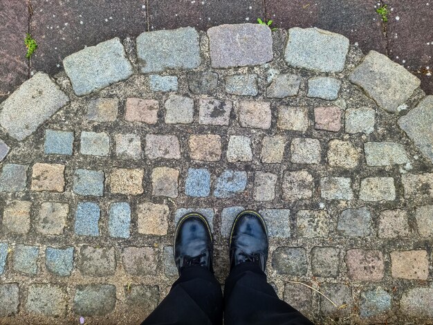 Foto zwei schwarze schuhe und beine auf einer kopfsteinpflasteroberfläche - top-view-konzept