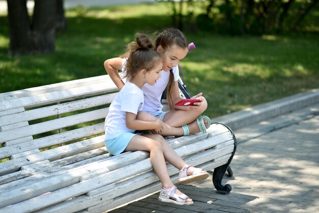 Zwei Schwestermädchen sitzen auf einer Bank und kommunizieren über ein Gadget