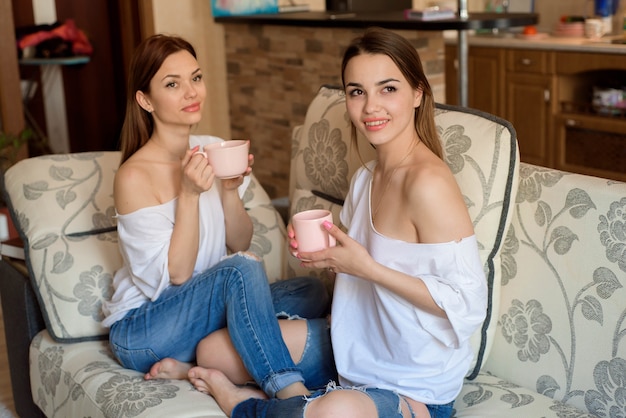 Zwei Schwestern auf dem Sofa mit Tassen Tee in den Händen