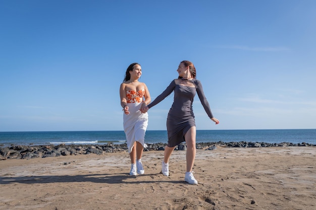 Zwei Schwestern halten Händchen und rennen am Strand entlang, Schwesterliebe