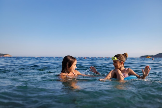 Zwei Schwestern in Badeanzügen spielen mit einem aufblasbaren Ring im Meer