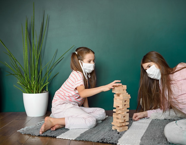 Zwei Schwestern in der medizinischen Maske, die ein Blockholzturmspiel spielen