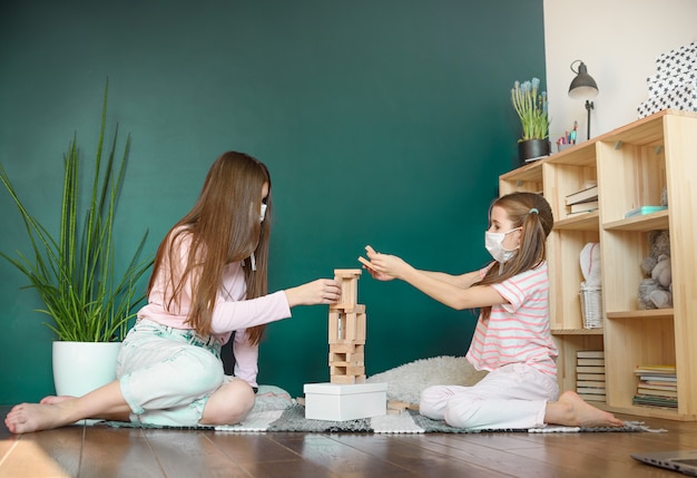 Zwei Schwestern in der medizinischen Maske, die ein Blockholzturmspiel spielen