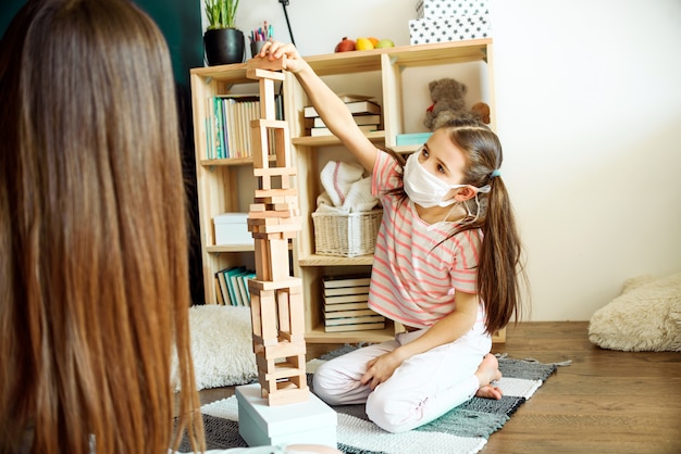 Zwei Schwestern in der medizinischen Maske, die ein Blockholzturmspiel spielen