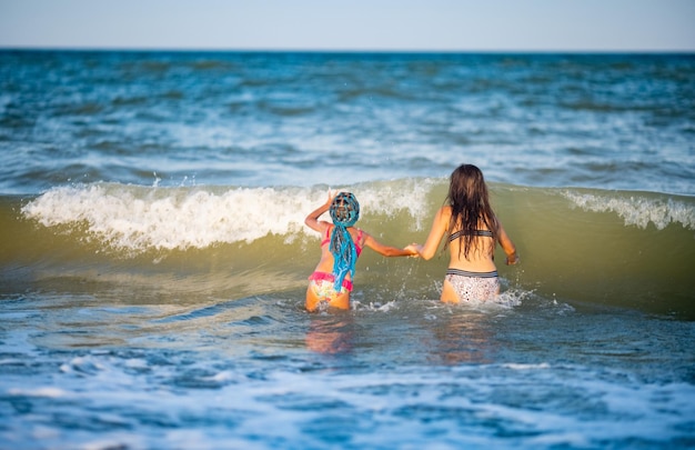 Zwei Schwestern in Sommerbadeanzügen spritzen an einem sonnigen Urlaubsabend in den Meereswellen auf Grund