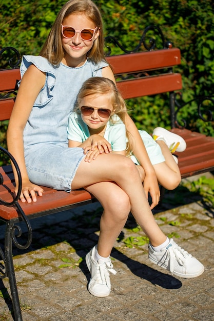 Zwei Schwestern mit Sonnenbrille sitzen im Sommer im Park auf einer Bank