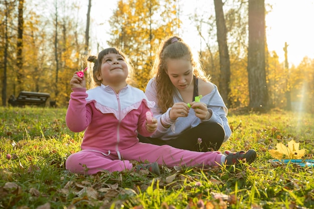 Zwei Schwestern parken im Herbst ein kleines Mädchen, das auf dem Boden sitzt, und ein anderes, das neben ihr sitzt