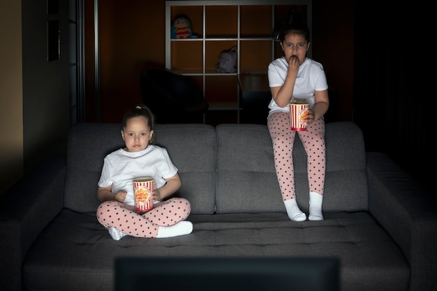 Zwei Schwestern schauen sich am Abend interessiert auf der Couch in einem dunklen Raum eine Fernsehsendung im Fernsehen an.