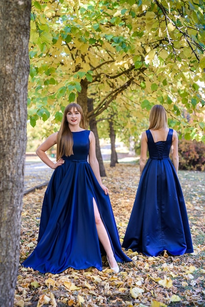 Zwei sehr schöne junge Damen in modischen blauen Kleidern im Herbstpark.