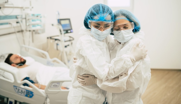 Zwei selbstbewusste Ärzte in Schutzanzügen stehen auf dem Hintergrund eines Patienten mit Coronavirus