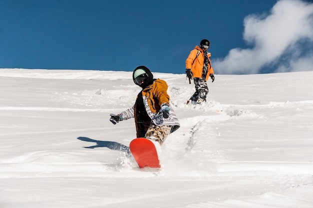 Zwei Snowboarder in Sportkleidung fahren den Berghang hinunter