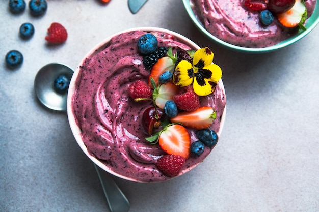 Zwei sommerliche Acai-Smoothie-Schalen mit Erdbeeren Blaubeeren auf grauem Betonhintergrund Frühstücksschüssel mit Obst und Müsli Nahaufnahme Draufsicht gesunde Ernährung