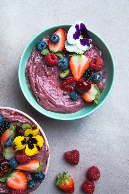 Zwei sommerliche Acai-Smoothie-Schalen mit Erdbeeren, Heidelbeeren auf grauem Betonhintergrund Frühstücksschüssel mit Obst und Müsli Nahaufnahme Draufsicht gesunde Ernährung