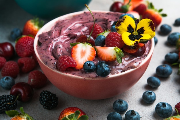 Zwei sommerliche Acai-Smoothie-Schalen mit Erdbeeren, Heidelbeeren auf grauem Betonhintergrund Frühstücksschüssel mit Obst und Müsli Nahaufnahme Draufsicht gesunde Ernährung