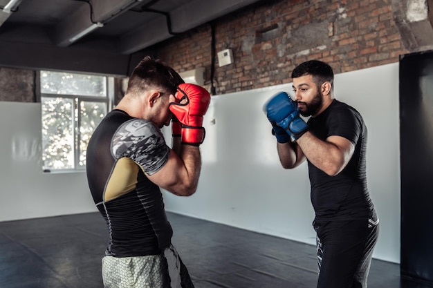 Zwei Sparringspartner eines Kickboxers in Boxhandschuhen üben in einer Sporthalle Kicks